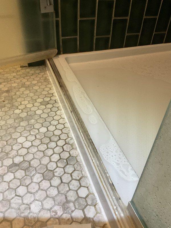 Inspected bathroom shower for reported leak occurring during shower operation. Utilized level tool to verify proper alignment of tub and tile interface. Identified water intrusion point at shower door track where green tile wall meets tub edge. Applied waterproof sealant to prevent further leakage.