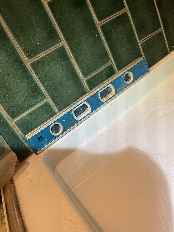 Inspected bathroom shower for reported leak occurring during shower operation. Utilized level tool to verify proper alignment of tub and tile interface. Identified water intrusion point at shower door track where green tile wall meets tub edge. Applied waterproof sealant to prevent further leakage.