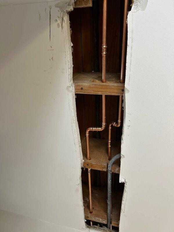 Accessed plumbing system by opening drywall section to expose copper water lines and PVC pipes within the wall cavity. Performed necessary repairs on the exposed plumbing infrastructure as sold by Jon, then documented the repair area with detailed photos showing both the exposed piping system and surrounding wall structure.