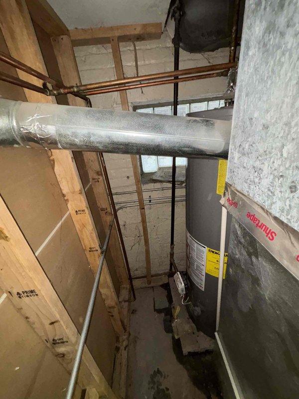 Conducted an inspection of a malfunctioning water heater in an unfinished basement after customer reported no hot water. Observed significant corrosion on copper pipe configuration and valve components with visible water damage on the concrete floor below, indicating active leakage. Provided customer with replacement options for the aging unit, noting the current installation would require updating to meet current code requirements.