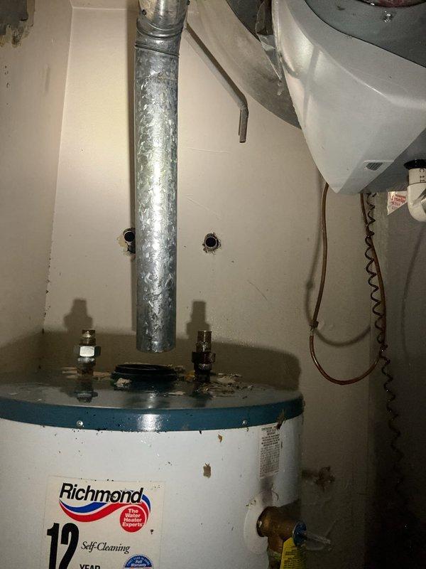 Responded to emergency call for a burst pipe that caused significant ceiling damage. Upon inspection, discovered water had leaked through the ceiling, creating a large hole and exposing structural joists. Repaired the burst pipe and installed a new Richmond water heater (12-year Self-Cleaning model) with proper copper line connections, venting, and valves to prevent future issues.