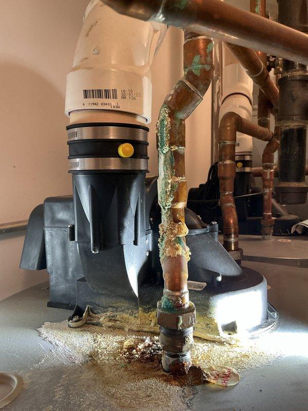 Responded to homeowner's report of beeping noise suspected to be from sump pump or water heater. Inspection revealed significant corrosion and mineral deposits on copper plumbing components, particularly at pipe joints, indicating ongoing leakage issues. Observed oxidation on copper pipes with greenish-blue patina and crusty accumulations, with additional rust noted on metal escutcheon plate where PVC drain pipe enters wall.
