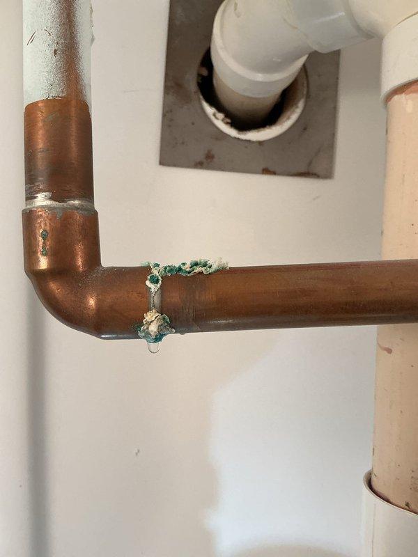 Responded to homeowner's report of beeping noise suspected to be from sump pump or water heater. Inspection revealed significant corrosion and mineral deposits on copper plumbing components, particularly at pipe joints, indicating ongoing leakage issues. Observed oxidation on copper pipes with greenish-blue patina and crusty accumulations, with additional rust noted on metal escutcheon plate where PVC drain pipe enters wall.