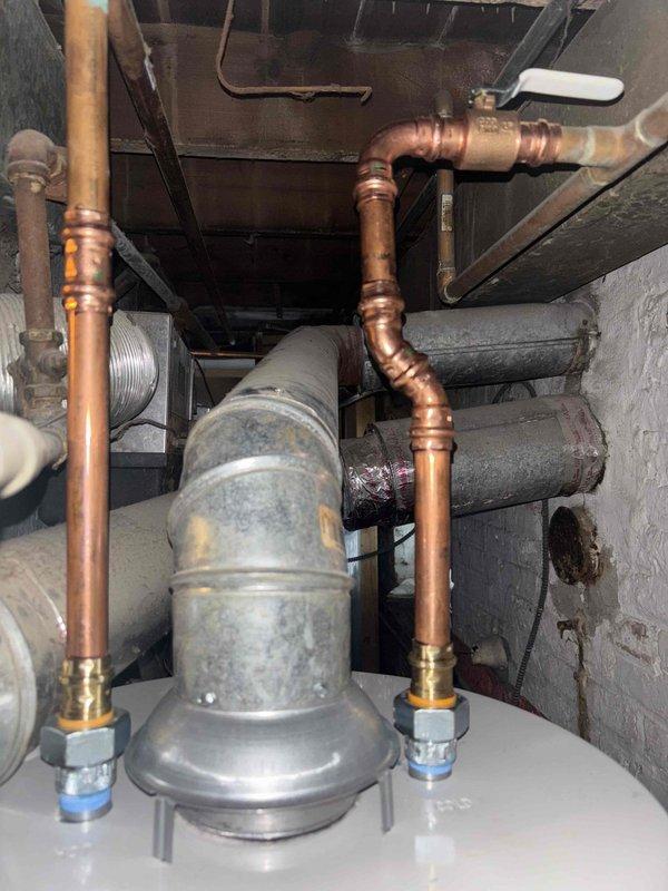 Completed installation of a 40-gallon atmospheric water heater in a confined basement utility area. Removed old unit showing signs of leakage, installed new heater with proper copper pipe connections, and ensured proper venting through existing galvanized ductwork. Installation required specialized positioning due to extremely tight space constraints.