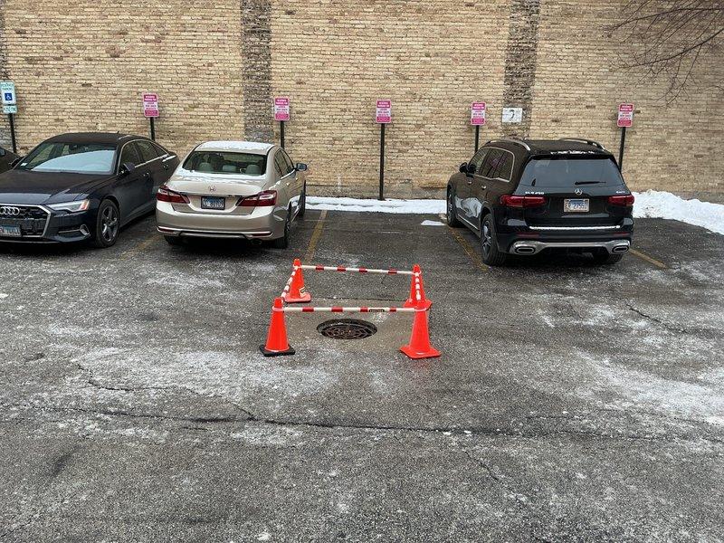 Performed site inspection of parking lot catch basin reported to be sinking and discharging sandy material despite previous repair work by another contractor. Visual assessment confirmed compromised drain structure with surrounding concrete showing signs of deterioration and cracking. Documented current condition with photographs showing the affected area currently cordoned off with safety cones and caution tape. Prepared estimate for complete catch basin replacement as requested by customer.
