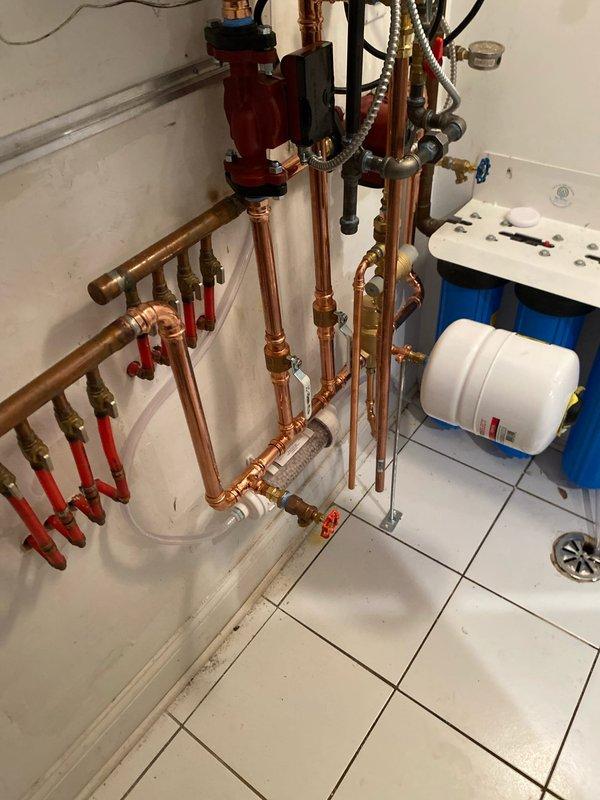 Successfully installed a new Navien tankless water heater system after the client's previous boiler was condemned. Work included comprehensive copper pipe installation with multiple valves and connectors, integration of a red circulator pump, and proper connection of PVC vent pipes for exhaust and intake. System was completed with installation of an expansion tank and water filtration components, all professionally mounted and tested for optimal performance.