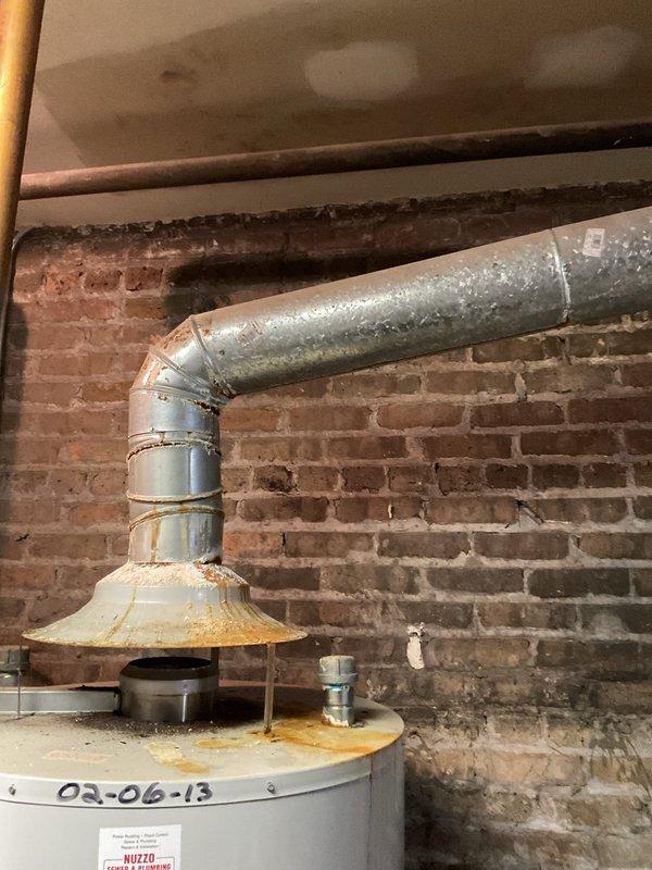 Inspected 2012 water heater exhibiting significant corrosion at base and leakage from top connection. Observed rust around vent pipe flange and aging expansion tank with copper supply lines. Recommended complete replacement of unit due to age, rust damage, and active leaking.