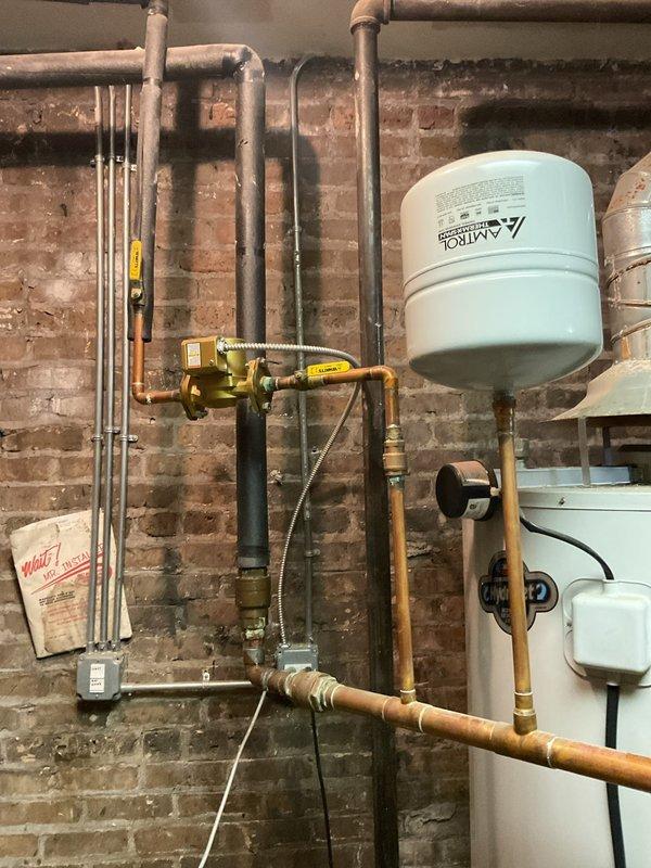 Inspected 2012 water heater exhibiting significant corrosion at base and leakage from top connection. Observed rust around vent pipe flange and aging expansion tank with copper supply lines. Recommended complete replacement of unit due to age, rust damage, and active leaking.