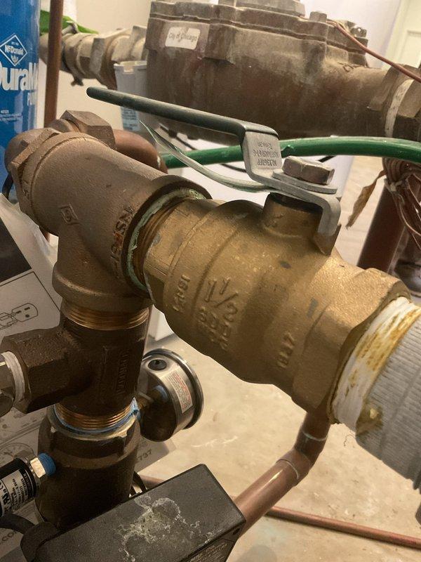 Installed vibration connectors on residential water booster pump system featuring an AMTROL expansion tank (model #170444C070PC2-5). Inspected existing brass pipe fittings and 1½" ball valve for proper operation, addressing mineral buildup on lower connection points to ensure optimal performance and reduce system noise.