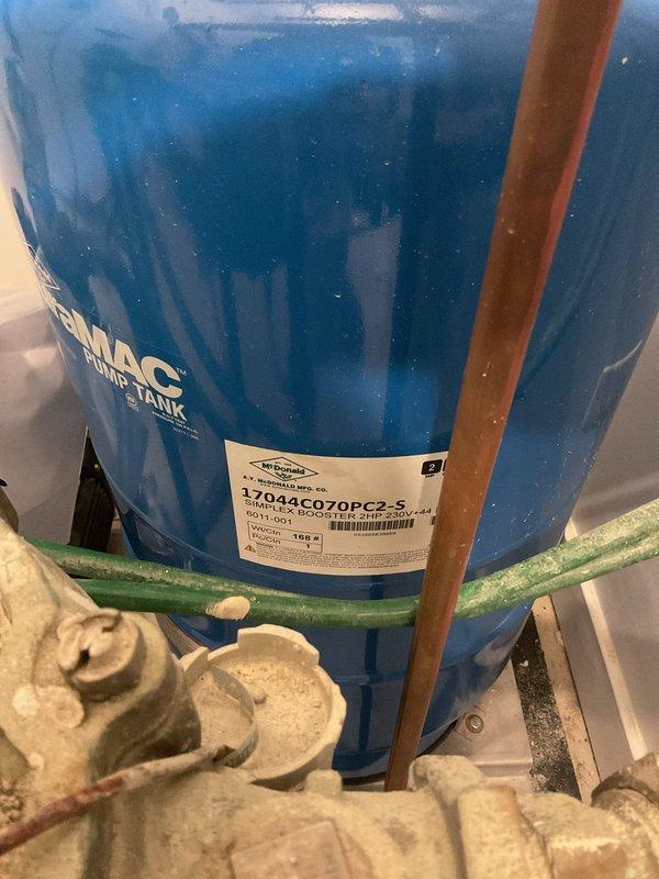 Installed vibration connectors on residential water booster pump system featuring an AMTROL expansion tank (model #170444C070PC2-5). Inspected existing brass pipe fittings and 1½" ball valve for proper operation, addressing mineral buildup on lower connection points to ensure optimal performance and reduce system noise.
