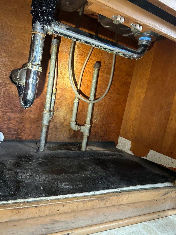 Replaced severely corroded metal P-trap assembly showing significant black mold and water damage with new PVC drain assembly. Installed complete P-trap configuration with proper threaded connections to address persistent sink clog and eliminate leakage that had caused cabinet base deterioration.
