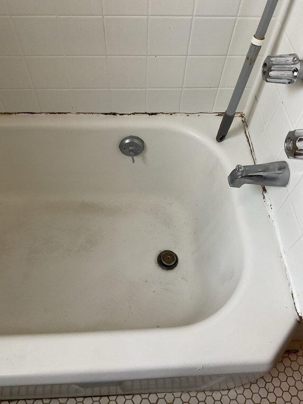 Responded to service request for clogged shower drain affecting sink drainage. Inspection revealed significant buildup in the bathtub drain system with visible staining and discoloration at tub-wall junction. Performed drain cleaning service to clear blockage in the interconnected bathroom drainage system, restoring proper water flow to both shower and sink fixtures.