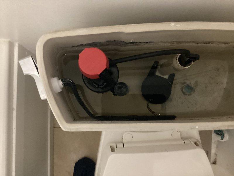 Responded to service call for malfunctioning toilet. Inspected TOTO toilet and internal tank components, noting mineral buildup and staining on the fill valve assembly. Serviced the toilet mechanism, focusing on the red float valve component and associated plumbing to restore proper functionality.