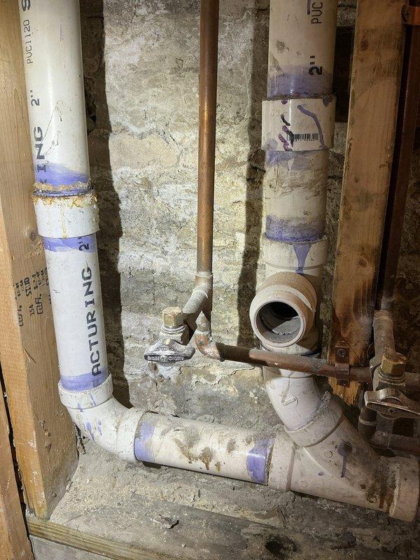 Performed inspection of shared sewage line with leaking PVC coupling before connection to main underground sewage line. Observed deteriorated pipe connections in basement utility area with visible moisture damage. Area shows partial renovation with exposed wall studs and insulation, requiring repair of the compromised coupling to prevent further leakage and potential structural damage.