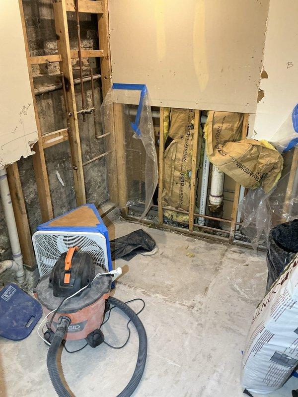 Performed inspection of shared sewage line with leaking PVC coupling before connection to main underground sewage line. Observed deteriorated pipe connections in basement utility area with visible moisture damage. Area shows partial renovation with exposed wall studs and insulation, requiring repair of the compromised coupling to prevent further leakage and potential structural damage.