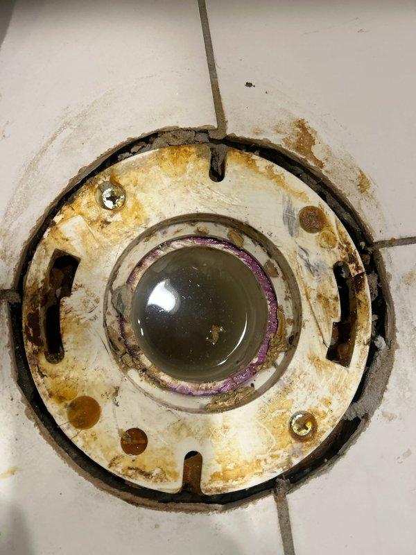 Technician removed toilet to inspect reported flush and clog issues, discovering a severely deteriorated toilet flange with extensive rust and mineral buildup. After assessment, replaced the corroded metal flange and installed new wax ring to restore proper seal and flushing functionality.