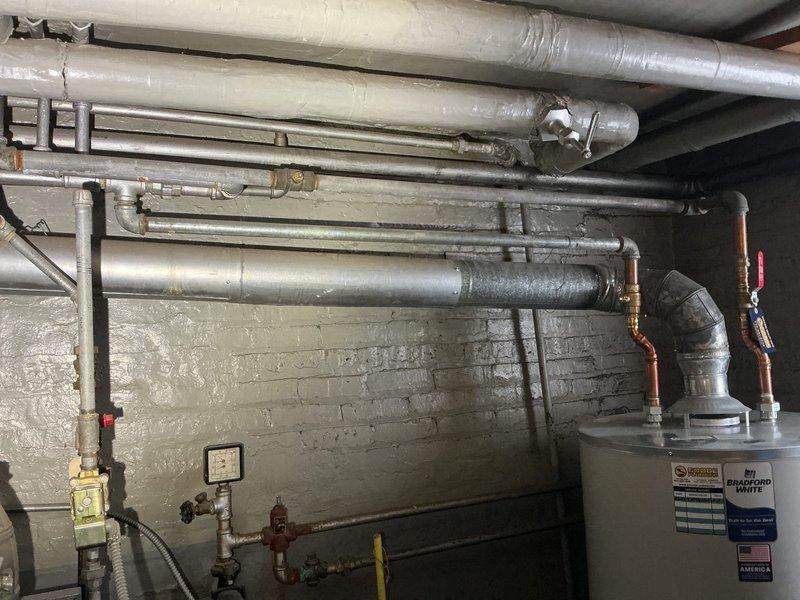 Responded to service call transferred from Brian to Jon. Inspected residential plumbing system where significant wood deterioration and water damage was observed around the PVC drainage system with P-trap configuration. Documented condition of Bradford White water heater installation and associated piping infrastructure including copper supply lines, metal exhaust venting, and pressure gauge components.