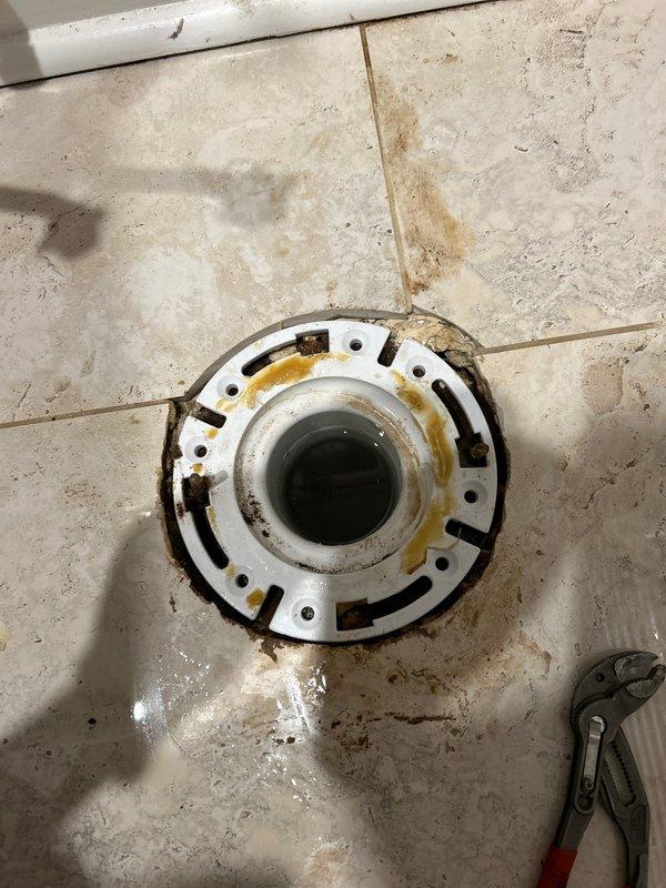 Responded to emergency water leak call and identified deteriorated toilet flange with significant corrosion as the source of leakage. Removed damaged wax ring, cleaned residual caulking material from floor drain area, and installed new toilet flange and wax seal to restore proper function and prevent further water damage.