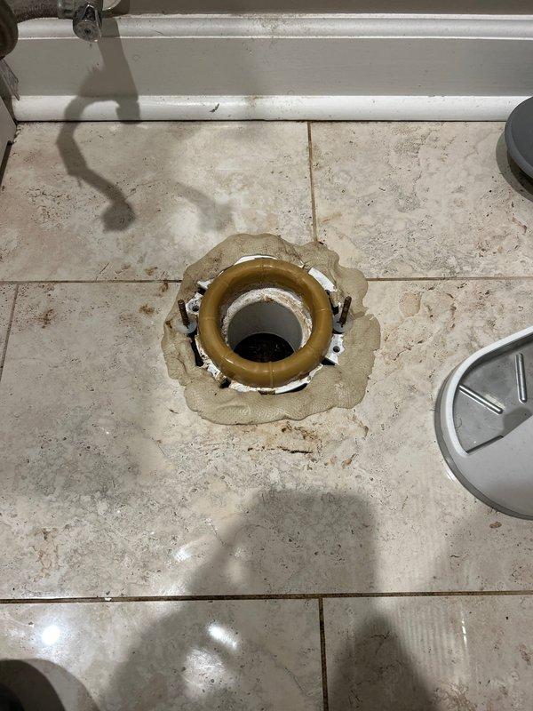 Responded to emergency water leak call and identified deteriorated toilet flange with significant corrosion as the source of leakage. Removed damaged wax ring, cleaned residual caulking material from floor drain area, and installed new toilet flange and wax seal to restore proper function and prevent further water damage.
