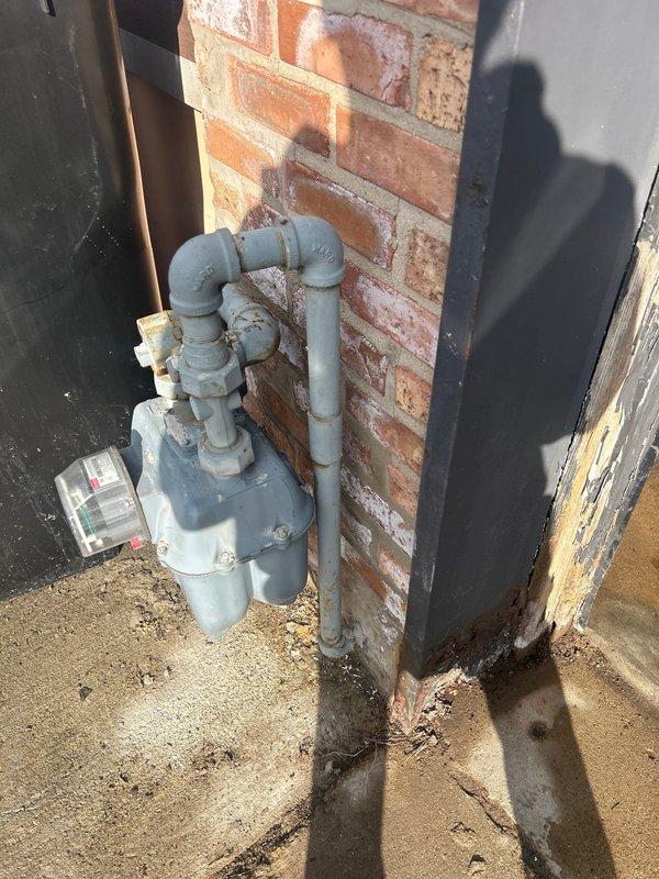 Conducted comprehensive assessment of existing plumbing infrastructure, including inspection of corroded metal supply pipes and gas meter installation against brick wall. Documented condition of vertical rusty pipe system, PVC connections, and gas meter configuration with associated piping. Photos taken to document current state for estimate purposes.