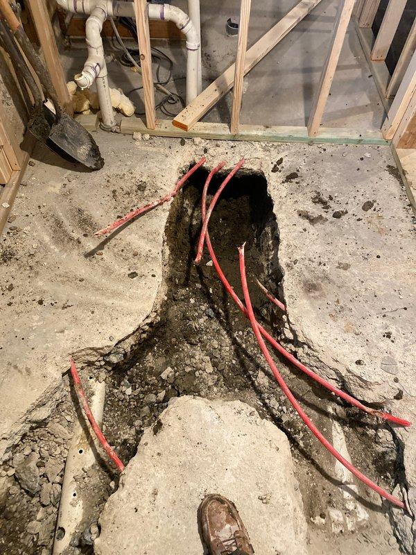 Excavated concrete floor to access and install PEX plumbing lines as part of basement renovation project. Installed multiple red PEX pipes through prepared trench, coordinating with ongoing construction. Project remains in progress pending final design approval and scheduling with general contractor.