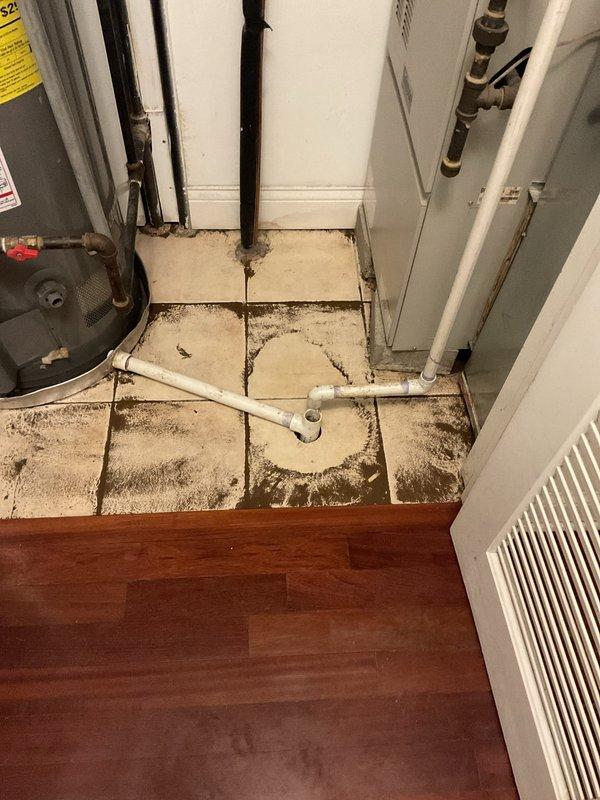 Responded to recurring backup issue in floor drain connected to washing machine. Observed significant mineral deposits and staining around floor drain with white PVC piping. Inspected plumbing configuration including copper pipes and drainage system in utility area. Noted potential water damage to surrounding tile flooring that may be contributing to drainage problems.