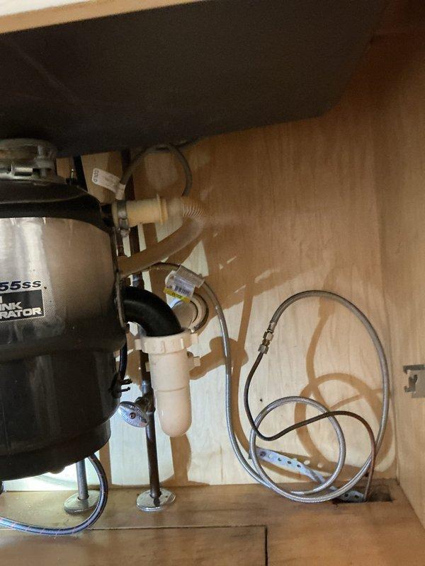 Inspected dishwasher plumbing connection issue reported by manufacturer's technician. Examined under-sink configuration including garbage disposal (InSinkErator 55SS model) and associated PVC drainage components. Verified all connection points between dishwasher drain line and disposal unit. Confirmed proper installation and functionality of plumbing components with no visible leaks or blockages detected.