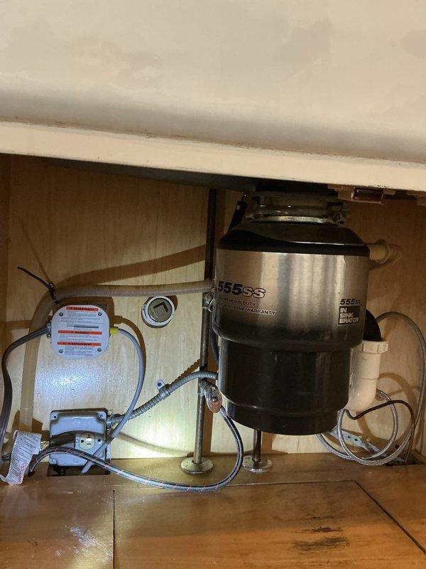 Inspected dishwasher plumbing connection issue reported by manufacturer's technician. Examined under-sink configuration including garbage disposal (InSinkErator 55SS model) and associated PVC drainage components. Verified all connection points between dishwasher drain line and disposal unit. Confirmed proper installation and functionality of plumbing components with no visible leaks or blockages detected.