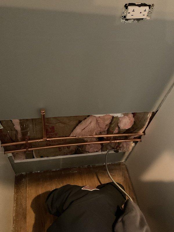 Completed sold repair job involving copper pipe work in a utility installation area. Accessed plumbing system through ceiling/wall opening, working around existing electrical components and insulation. Photo documentation taken of repair site before and after service completion.