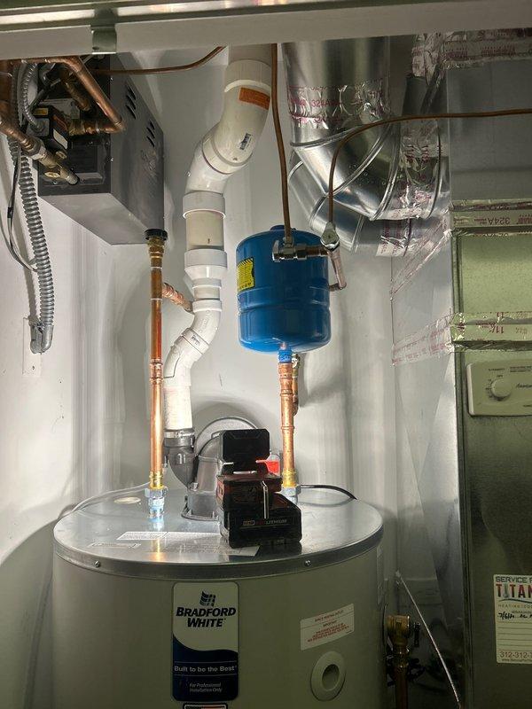 Installed Bradford White power vent water heater with blue expansion tank and complete copper piping connections. System includes proper PVC venting configuration and all necessary valves for operation. Installation completed and unit functioning as designed.