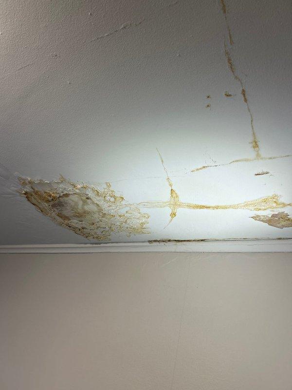 Performed water leak investigation in second-floor bathroom affecting first-floor ceiling. Identified significant water damage with yellowish-brown staining and ceiling material deterioration. Inspection revealed compromised drywall/plaster with exposure of wooden structural elements and visible plumbing components, confirming persistent water infiltration from the tub area as suspected by customer.