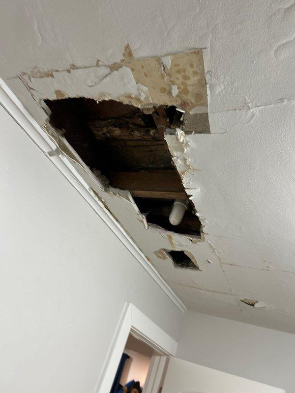 Performed water leak investigation in second-floor bathroom affecting first-floor ceiling. Identified significant water damage with yellowish-brown staining and ceiling material deterioration. Inspection revealed compromised drywall/plaster with exposure of wooden structural elements and visible plumbing components, confirming persistent water infiltration from the tub area as suspected by customer.