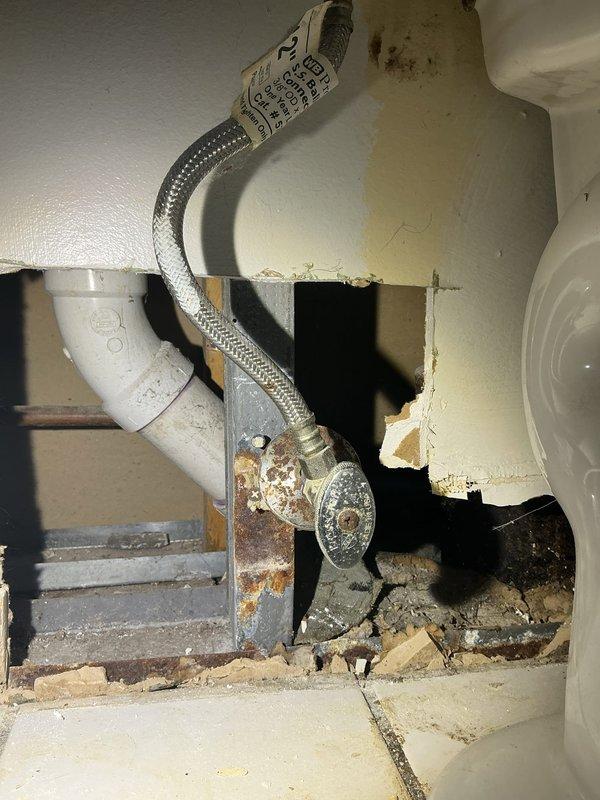 Conducted inspection of bathroom plumbing for requested drain line relocation and water line modifications during customer's remodel project. Observed existing fixtures showing significant corrosion and mineral buildup on valve stems, with damaged wall material surrounding connection points. Documented deteriorated PVC drain components and aging supply lines that will require replacement during the repositioning work.