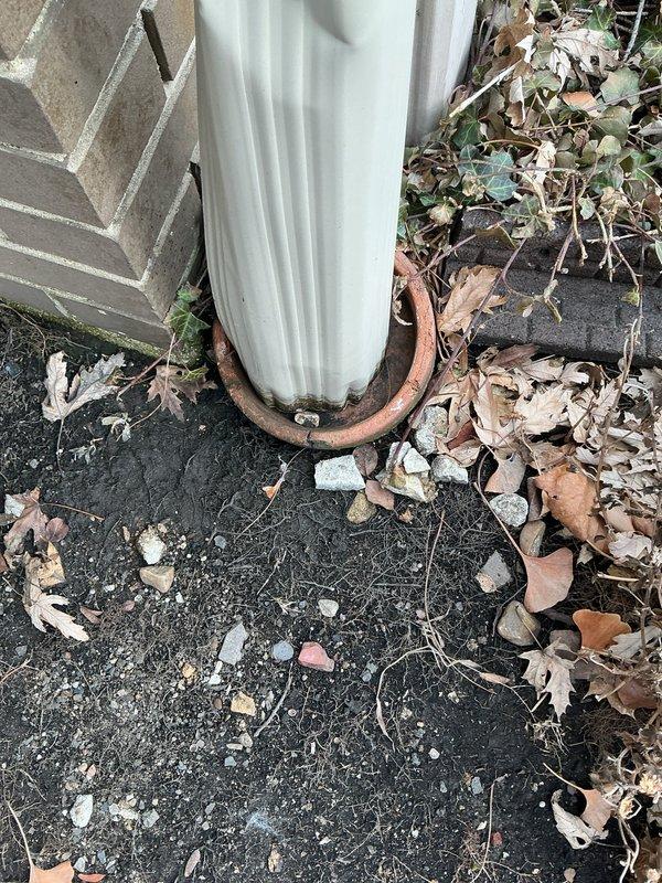 Inspected exterior downspout drainage system causing front yard flooding during rainfall. Identified significant deterioration at pipe seam with visible rust and corrosion. Found drain base partially clogged with accumulated debris including leaves, soil, and plant matter, preventing proper water flow from the downspout.