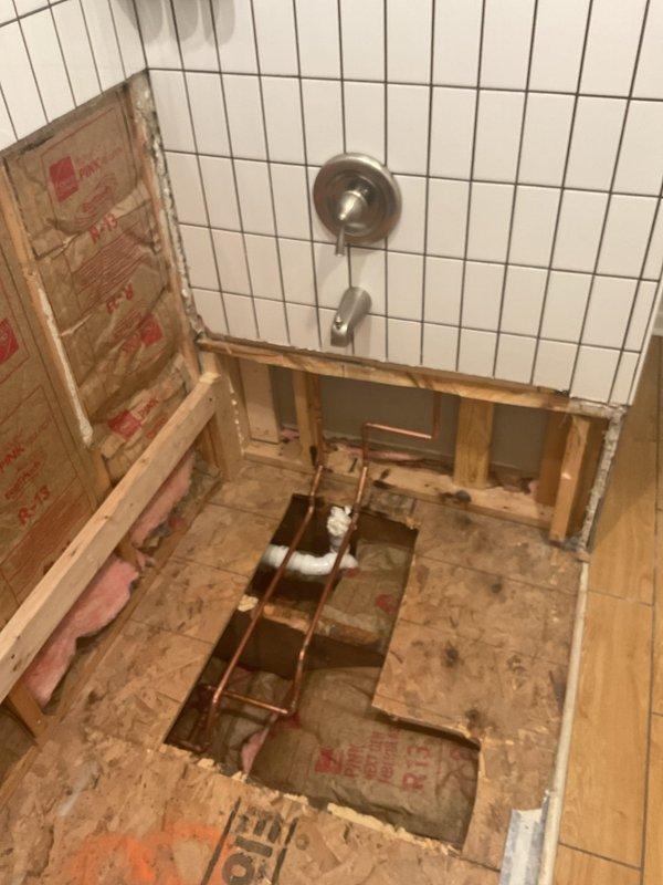Successfully installed new porcelain bathtub with chrome drain on wooden subfloor and connected to existing plumbing system. Mounted stainless steel faucet fixture on adjacent tiled wall and ensured proper drain connection through floor cutout to PVC drain pipe below.