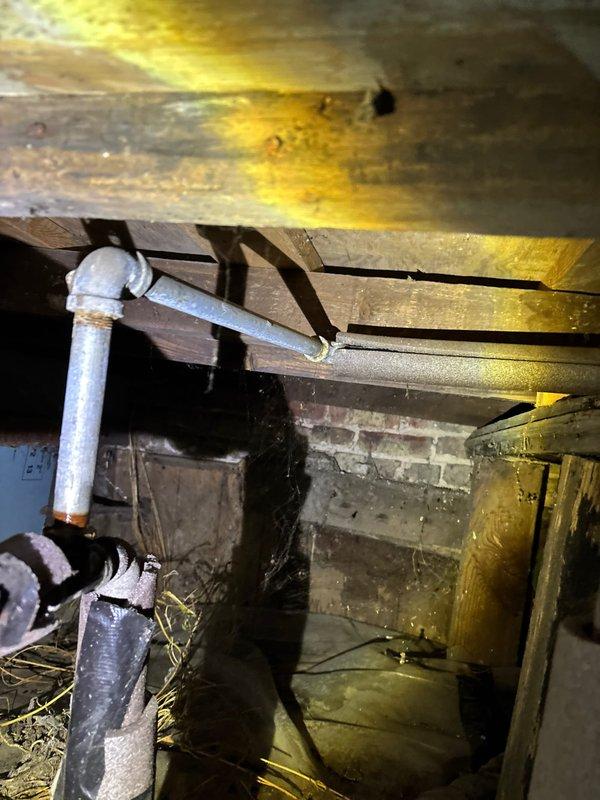 Performed emergency spot repair in restrictive crawl space, replacing corroded pipe junction where white PVC connected to older pipe showing significant discoloration. Installed new copper piping with appropriate shutoff valve, and secured all connection points with proper sealing technique as evidenced by the green marking tape at joints.