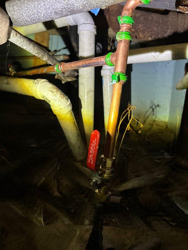 Performed emergency spot repair in restrictive crawl space, replacing corroded pipe junction where white PVC connected to older pipe showing significant discoloration. Installed new copper piping with appropriate shutoff valve, and secured all connection points with proper sealing technique as evidenced by the green marking tape at joints.