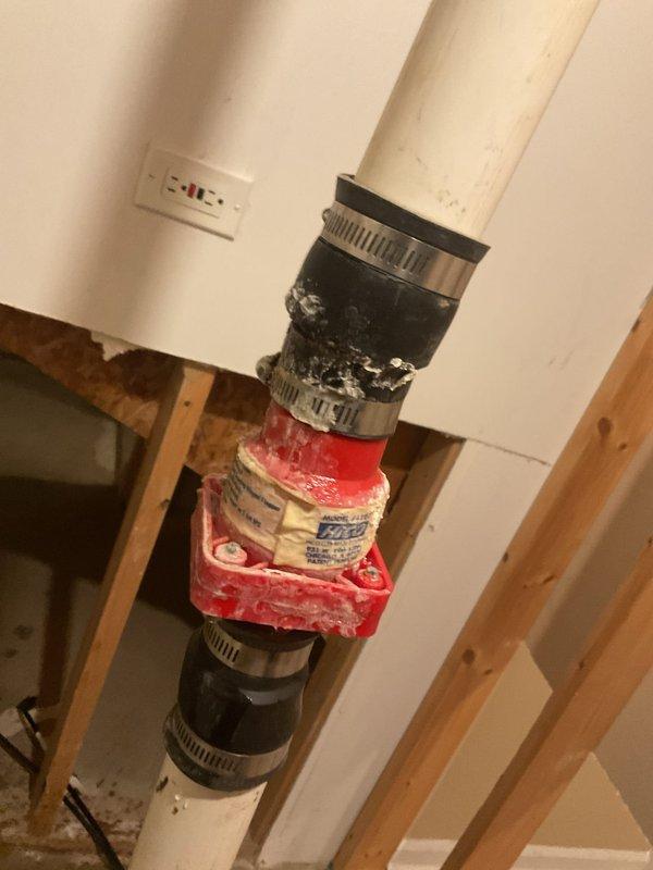 Performed inspection of sump pump system following customer's water restoration company assessment for potential mold issues. Examined toilet tank components showing significant mineral deposits and rust accumulation. Inspected PVC pipe assembly with red valve component and multiple metal hose clamps securing connections, noting proper installation despite surrounding unfinished wall area.