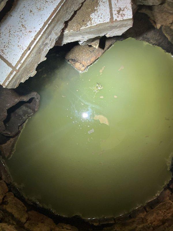 Responded to callback regarding standing water issue. Inspection revealed stagnant, contaminated water pooling in a damaged floor opening near plumbing infrastructure. Documented extensive water damage to surrounding tile and concrete, with visible staining on basement utility area walls where multiple black pipes and water heater are located.