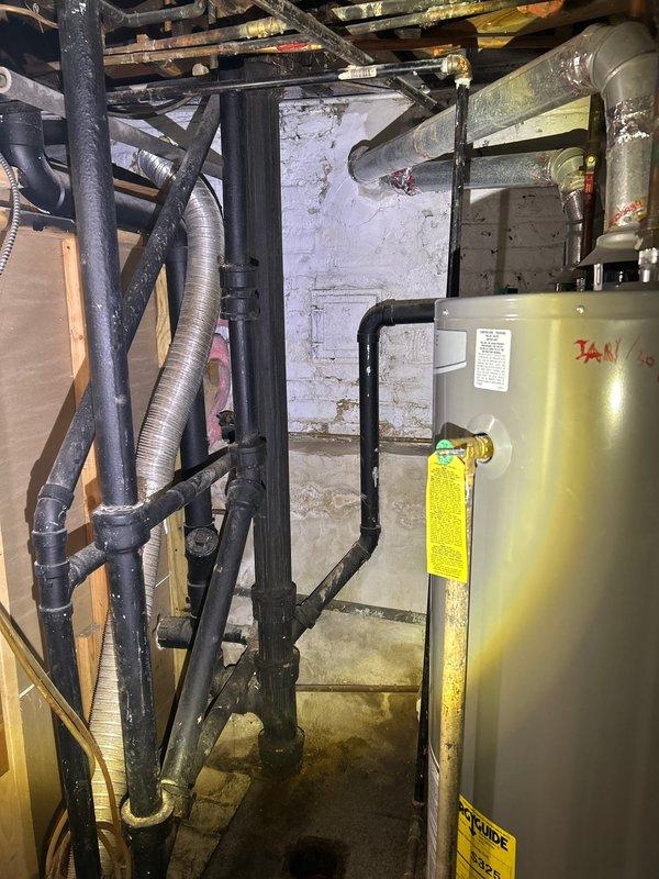 Located and identified source of water leak in basement, which was found to be originating from deteriorated connections between older metal piping and newer PVC components. Performed inspection of surrounding plumbing infrastructure including water heater system and associated piping network, documenting conditions with photographs for record.