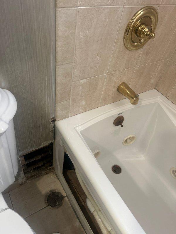 Performed inspection of bathroom for reported water leak from tub to ceiling below. Identified damaged wall section at tub-wall junction with exposed structural elements, potentially allowing water intrusion. Repaired deteriorated area, sealed gap between tub and wall, and verified proper drainage functionality to prevent further leakage to lower ceiling.