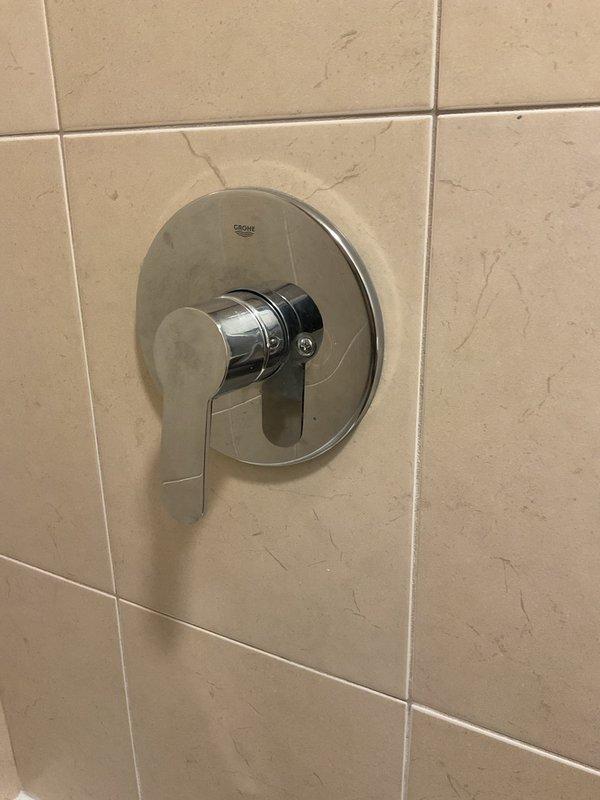 Diagnosed issue with Grohe shower valve handle that would not turn off. Observed chrome fixture with lever-style handle showing minor surface wear and surrounding beige tiles with hairline cracks. Appointment rescheduled to Monday after 10:30am due to parts availability; customer has temporarily shut off water supply to shower until repair can be completed.