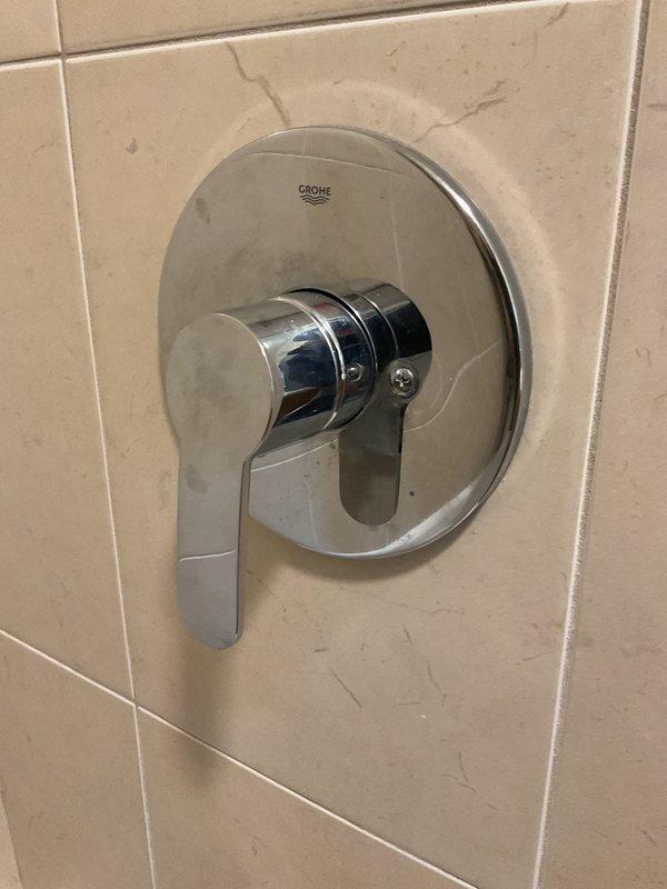 Diagnosed issue with Grohe shower valve handle that would not turn off. Observed chrome fixture with lever-style handle showing minor surface wear and surrounding beige tiles with hairline cracks. Appointment rescheduled to Monday after 10:30am due to parts availability; customer has temporarily shut off water supply to shower until repair can be completed.