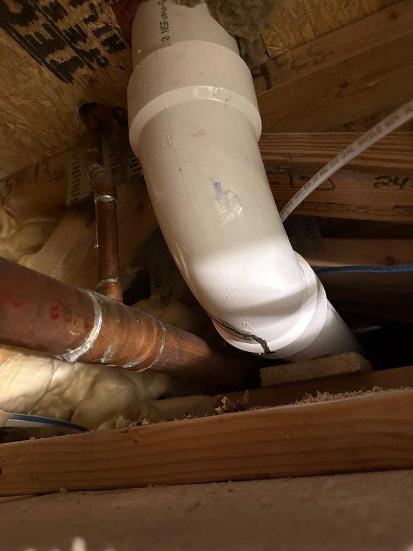 Investigated ceiling stain reported in shower area and identified a cracked PVC pipe elbow joint as the source of the leak. Accessed the plumbing through a wall opening, revealing damaged PVC fitting alongside copper supply lines. Documented the split in the curved section of the PVC pipe requiring replacement to resolve the water intrusion issue.