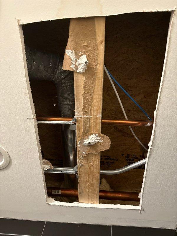 Investigated ceiling stain reported in shower area and identified a cracked PVC pipe elbow joint as the source of the leak. Accessed the plumbing through a wall opening, revealing damaged PVC fitting alongside copper supply lines. Documented the split in the curved section of the PVC pipe requiring replacement to resolve the water intrusion issue.