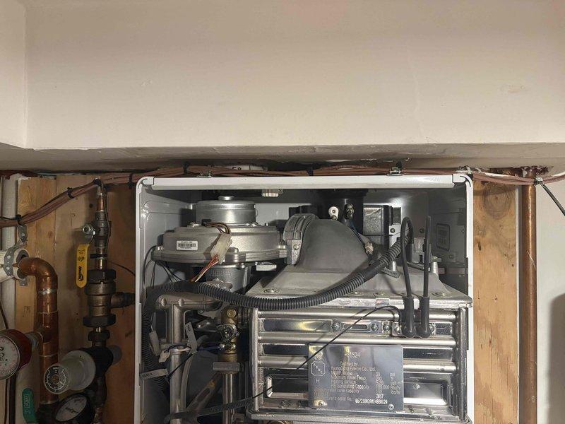 Diagnosed Navien tankless water heater system experiencing operational issues. Conducted comprehensive inspection of unit with front panel removed, examining internal components including control board, valves, and electrical connections. Took measurements of system configuration to evaluate proper installation parameters and determine appropriate repair or replacement options.