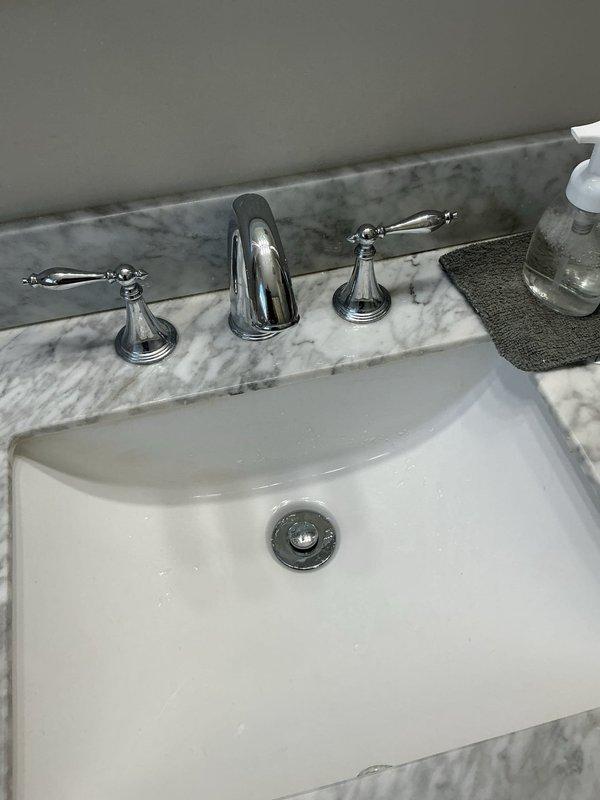 Responded to service call regarding a bathroom faucet leak reported to have started several months prior. Inspected undermount sink with widespread chrome faucet set in marble countertop. Customer had replacement faucet available if needed. Visual inspection of plumbing revealed gray plastic P-trap assembly with corrugated flexible piping and braided supply lines in good condition.