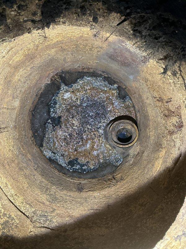 Performed callback inspection of downspout drainage system. Documented significant mineral buildup and corrosion in the circular drainage component, with extensive deterioration visible in the connecting pipe structure. Photographed evidence of standing water and sediment accumulation for estimate preparation to completely re-pipe downspout line to catch basin.