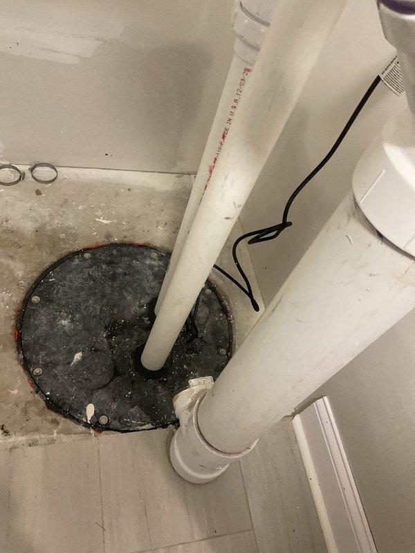 Responded to emergency service call for basement ejector pit overflow and non-functioning toilet. Inspected black circular sump pit lid with mounting bolts and connected PVC waste drainage system. Examined white PVC plumbing installation with multiple elbow joints and connections that showed signs of use with visible JM EAGLE markings.