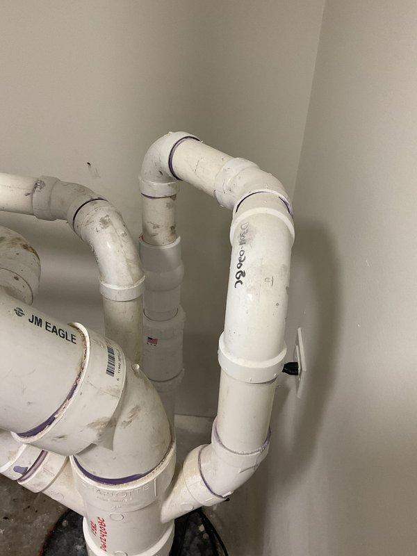 Responded to emergency service call for basement ejector pit overflow and non-functioning toilet. Inspected black circular sump pit lid with mounting bolts and connected PVC waste drainage system. Examined white PVC plumbing installation with multiple elbow joints and connections that showed signs of use with visible JM EAGLE markings.